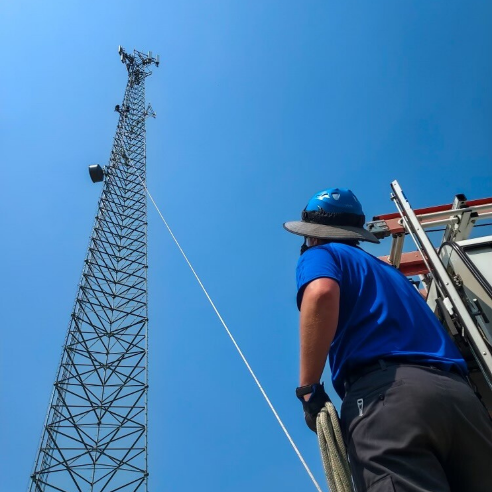 MetaLINK Technologies technician preparing to climb a tall communications tower under clear blue sky