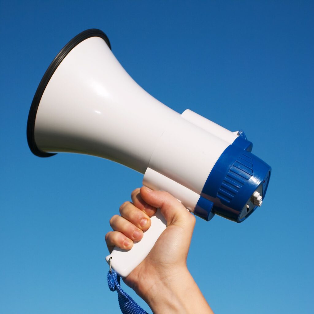 Hand holding a megaphone against a clear blue sky, representing MetaLINK Technologies' referral program promotion