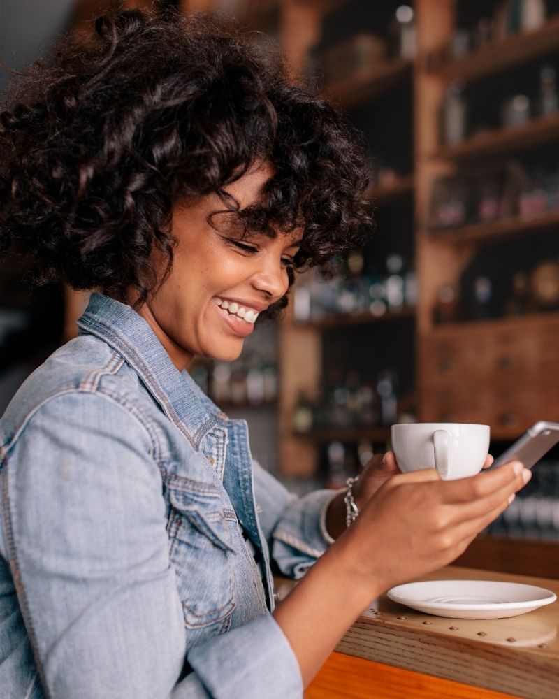 Smiling woman using wireless internet on smartphone at coffee shop