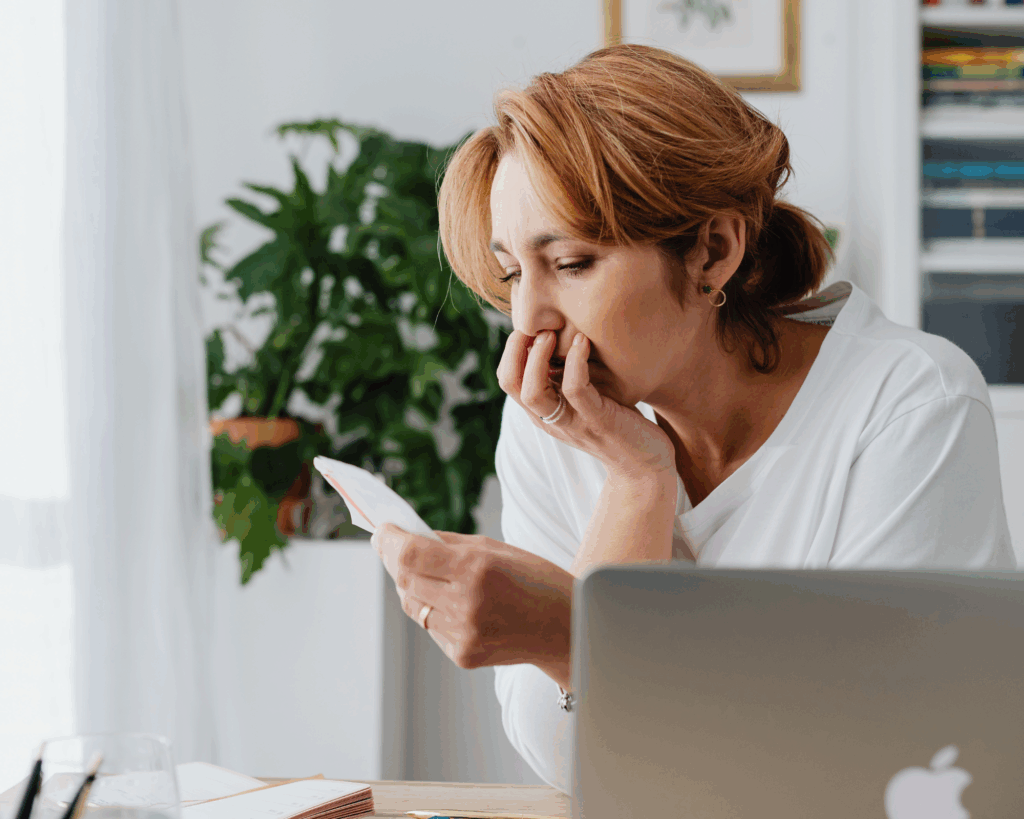 Worried woman looking at a bill while sitting at her desk with a laptop and paperwork