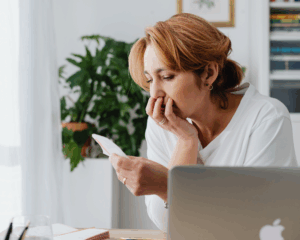 Worried woman looking at a bill while sitting at her desk with a laptop and paperwork