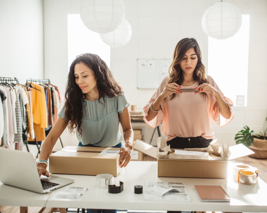 Two small business owners using a laptop and packing boxes for shipping in a home-based workspace