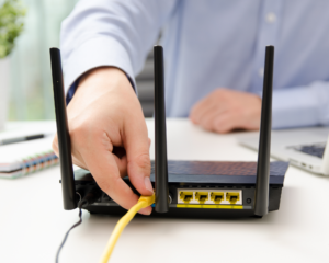 Person connecting ethernet cable to a WiFi router during home internet setup and installation