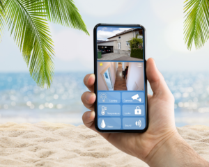 Smartphone displaying a home monitoring and security app while relaxing at the beach, showing how homeowners can stay connected to their property with reliable internet access during vacation.