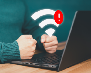 Frustrated customer with clenched fists at laptop showing WiFi symbol with red warning icon during internet outage