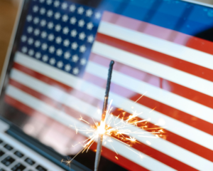 Laptop displaying an American flag with a lit sparkler in the foreground, symbolizing patriotic celebrations, Independence Day, and staying connected with reliable internet during the Fourth of July.