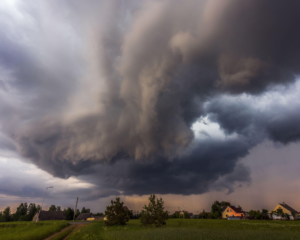 Dark storm clouds rolling over a rural neighborhood with houses and green fields, representing the need for reliable internet during severe weather