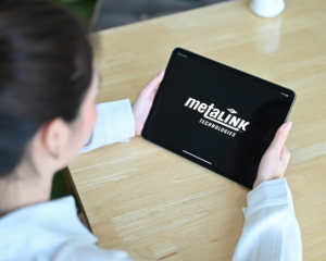 Over-the-shoulder view of a person holding a tablet displaying the MetaLINK Technologies logo on a black screen