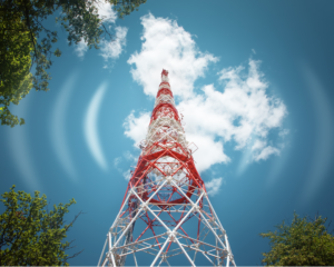 Red and white telecommunications tower with wireless signal waves, surrounded by trees under a blue sky, representing MetaLINK's internet service connecting rural communities.