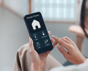 Close-up of a person holding a smartphone displaying a smart home control app with icons for lights, thermostat, locks, and security camera
