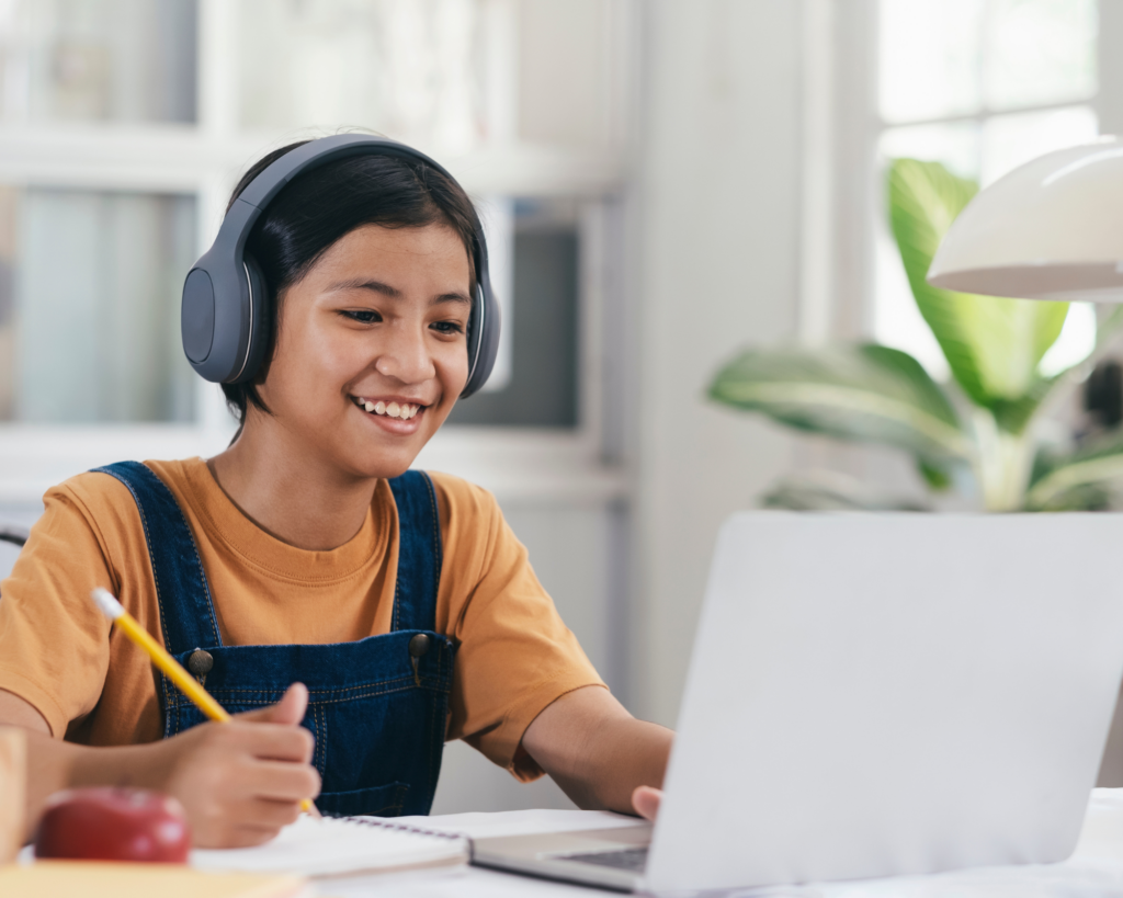 A smiling student wearing headphones and using a laptop during an online learning session.