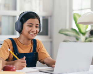 A smiling student wearing headphones and using a laptop during an online learning session.